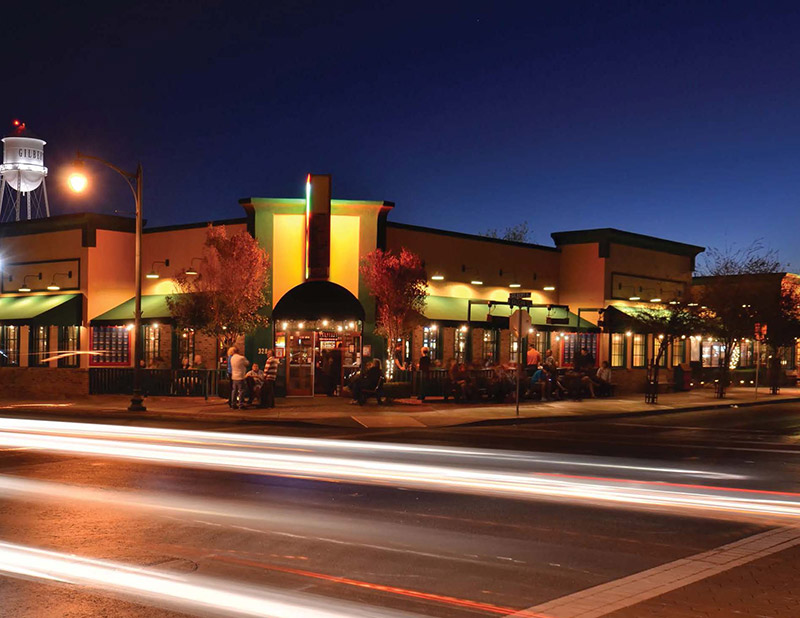 Outdoor night shot of Oregano's Pizza Bistro building. Blurred car lights across the photo. Gilbert water tower in the background.