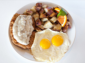 Plate with eggs, potatoes, and chicken fried steak with gravy.
